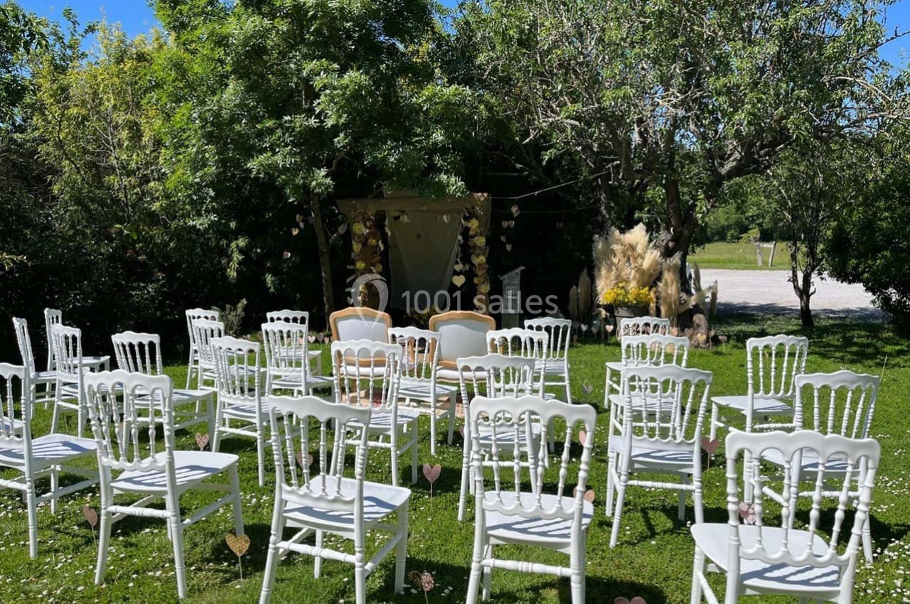 Location salle Sainte-Foy-d'Aigrefeuille (Haute-Garonne) - Les Ecuries de Ronsac #13 Chaises blanches disposées en rangées sur une pelouse, face à une arche décorée pour une cérémonie en plein air.