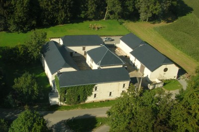 Cour pavée d'un bâtiment en pierre éclairé par des lumières extérieures, entouré d'arbres et de bâtiments annexes, de nuit.