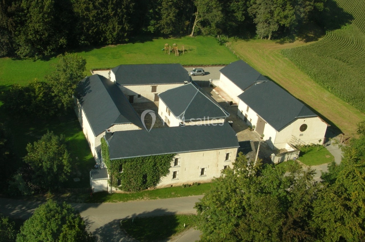 Vue aérienne d'un bâtiment en pierre en forme de U entouré de verdure et de routes de campagne.