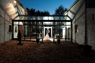 Cour pavée d'un bâtiment en pierre éclairé par des lumières extérieures, entouré d'arbres et de bâtiments annexes, de nuit.