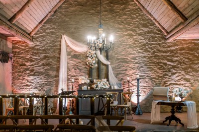 Cour pavée d'un bâtiment en pierre éclairé par des lumières extérieures, entouré d'arbres et de bâtiments annexes, de nuit.