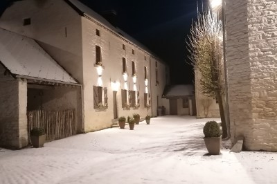 Cour pavée d'un bâtiment en pierre éclairé par des lumières extérieures, entouré d'arbres et de bâtiments annexes, de nuit.