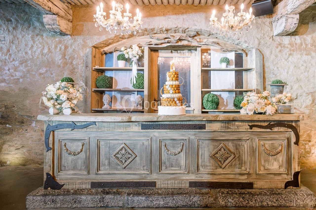 Comptoir en bois sculpté décoré de fleurs et d'une pièce montée, dans une salle en pierre éclairée par des lustres.