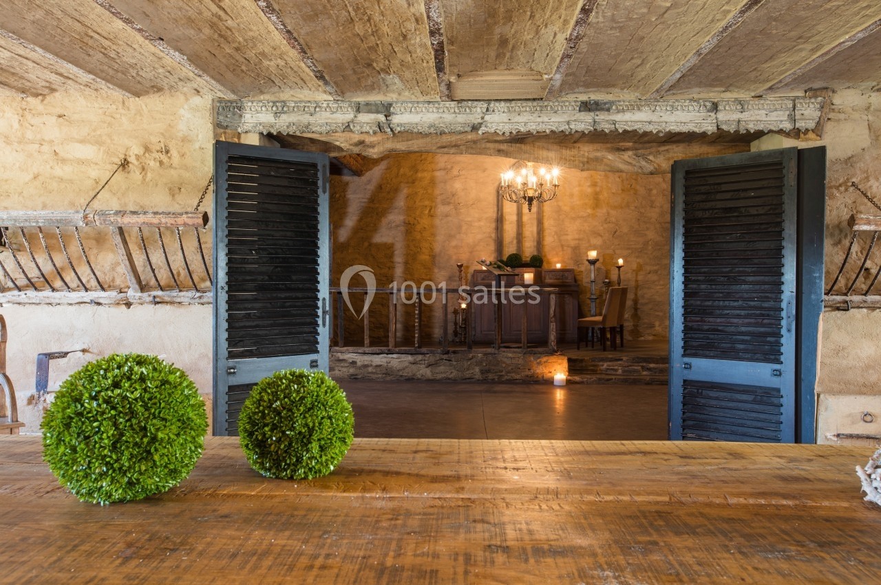 Vue intérieure d'une pièce rustique avec des murs en pierre, des volets en bois ouverts et une table décorée de boules…