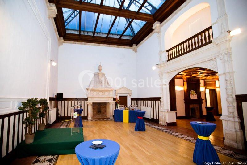 Location salle Saint-Romain-de-Colbosc (Seine-Maritime) - Château de Gromesnil #8 Salle lumineuse avec parquet, cheminée en pierre, tables hautes drapées de bleu et verrière en plafond.