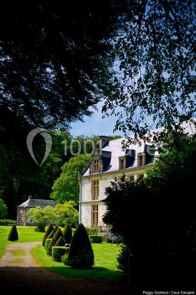 Location salle Saint-Romain-de-Colbosc (Seine-Maritime) - Château de Gromesnil #5 Manoir entouré de jardins verdoyants avec allée bordée de buissons taillés, sous un ciel partiellement dégagé.
