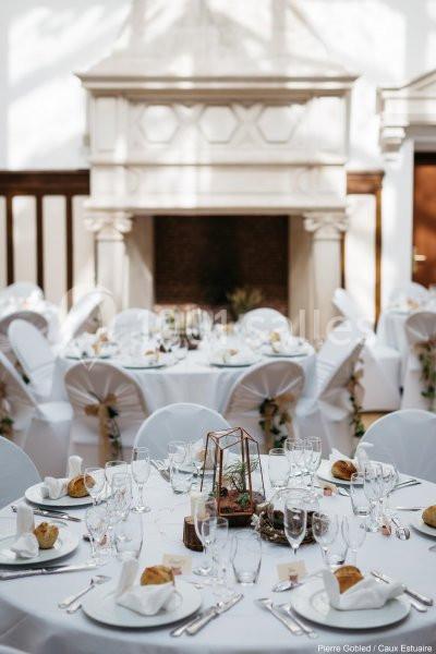 Location salle Saint-Romain-de-Colbosc (Seine-Maritime) - Château de Gromesnil #17 Tables rondes élégamment dressées avec nappes blanches, décorations florales et vaisselle, dans une salle lumineuse avec…