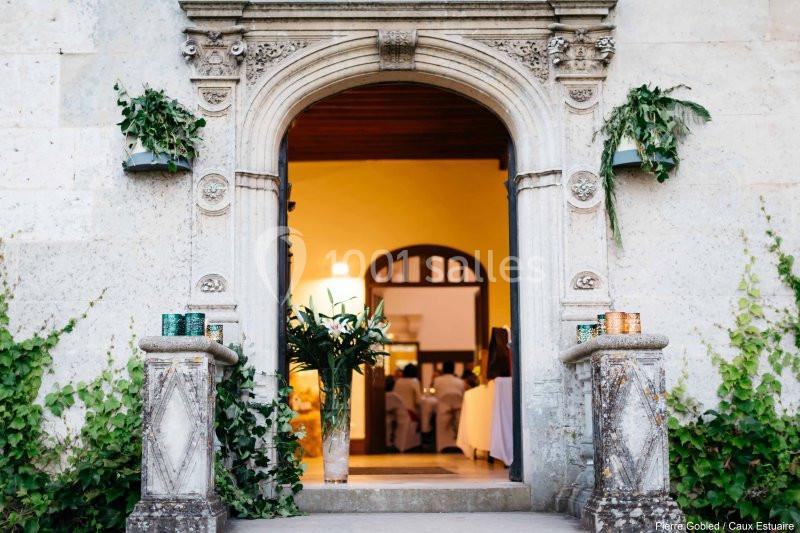 Location salle Saint-Romain-de-Colbosc (Seine-Maritime) - Château de Gromesnil #6 Entrée voûtée en pierre ornée de feuillages, donnant sur un intérieur éclairé avec des personnes en arrière-plan.