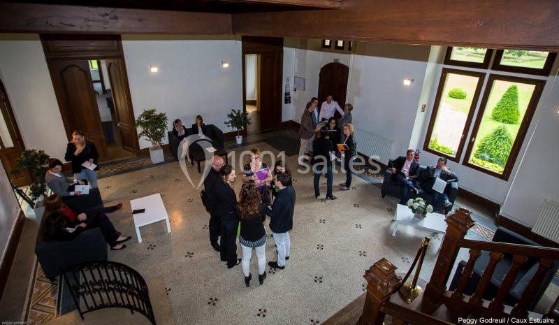 Groupe de personnes discutant dans un hall lumineux avec des fauteuils, des plantes et des grandes fenêtres.