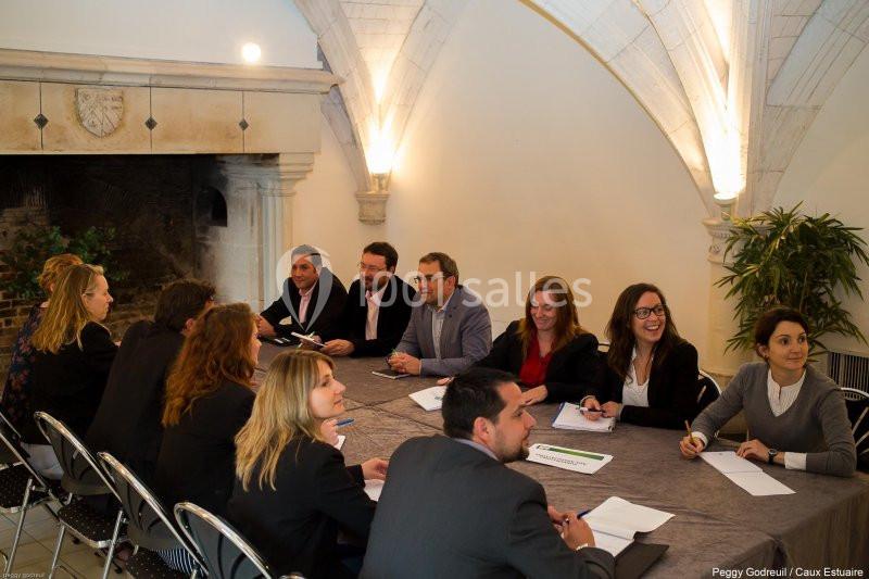 Des personnes en réunion autour d'une grande table dans une salle voûtée avec une cheminée en arrière-plan.