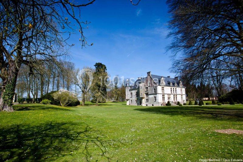 Manoir entouré d'un vaste parc verdoyant avec des arbres et un ciel bleu dégagé en arrière-plan.