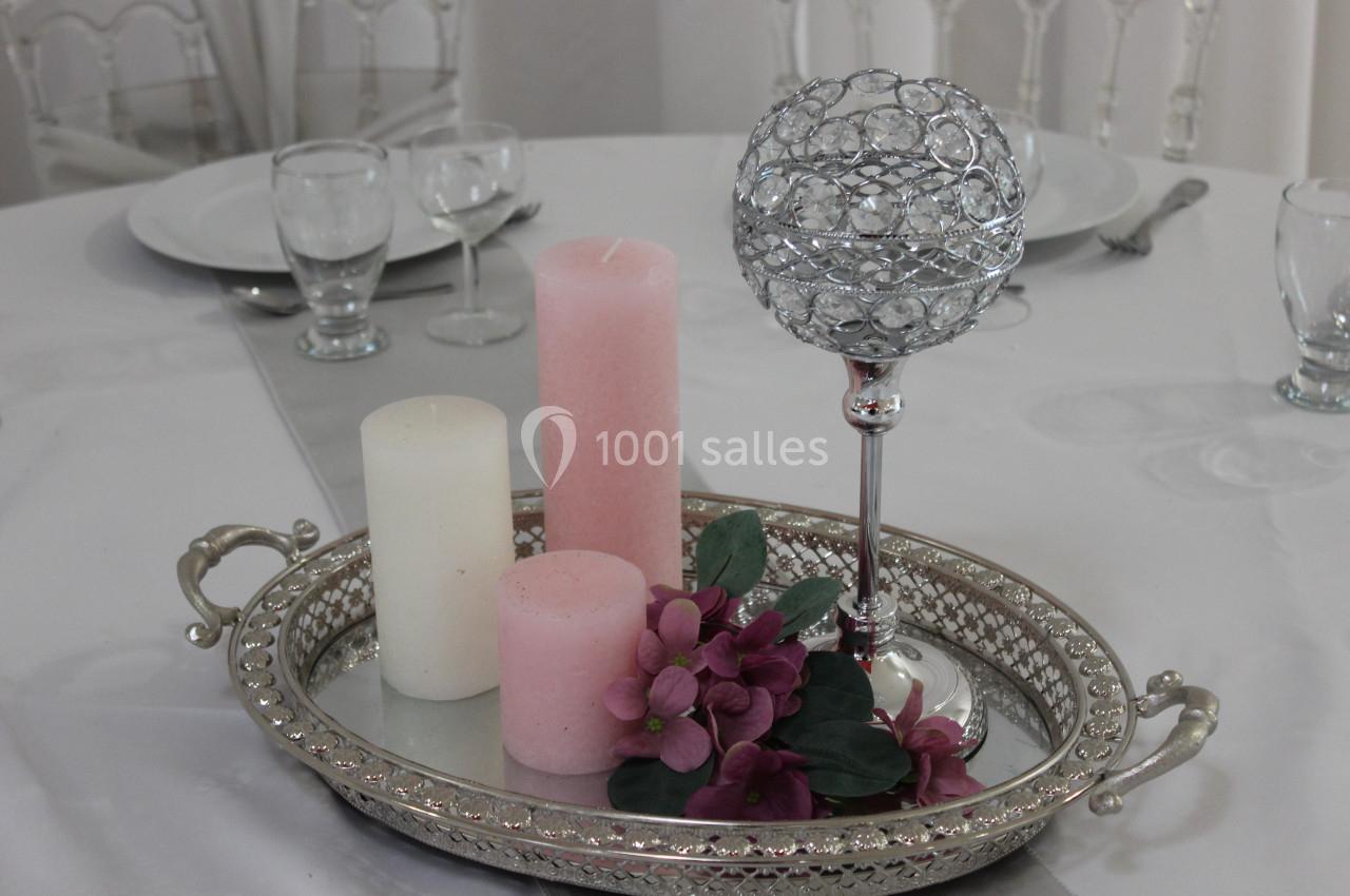 Centre de table avec bougies blanches et roses, fleurs violettes et support argenté décoratif sur une table dressée.