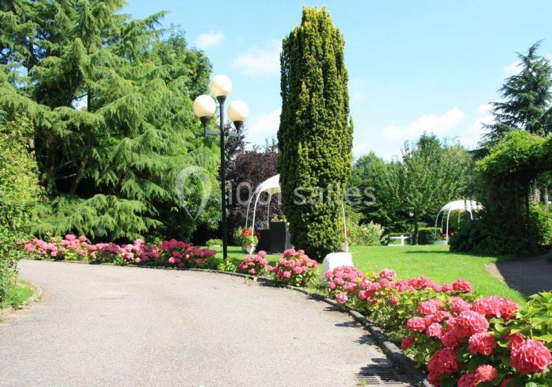 Allée bordée d'hortensias roses dans un jardin verdoyant avec arbres, pelouse et lampadaires.