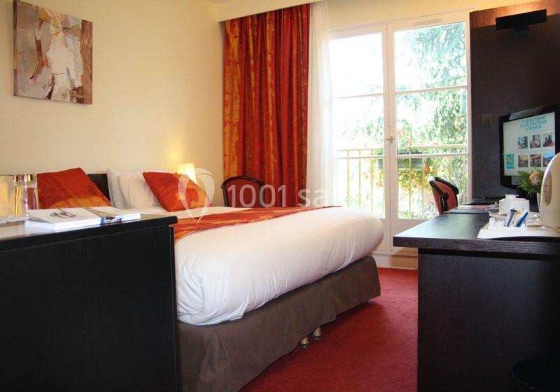 Chambre d'hôtel avec lit double, bureau, télévision, rideaux rouges et fenêtre donnant sur un espace arboré.