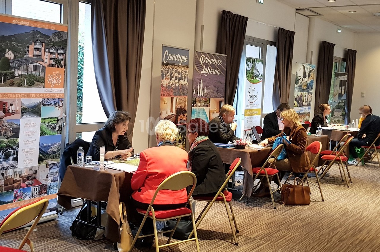 Des personnes discutent en face à face à des tables dans une salle avec des affiches promotionnelles en arrière-plan.