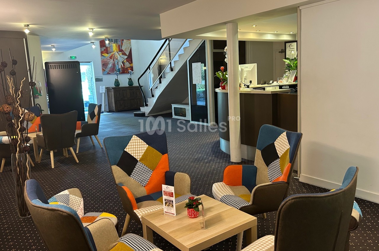 Espace d'accueil lumineux avec fauteuils colorés, table basse, comptoir de réception et escalier en arrière-plan.