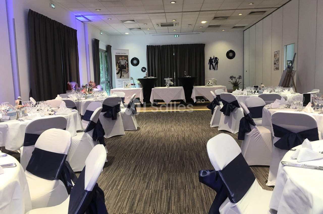 Salle de réception décorée avec des tables dressées, nappes blanches et nœuds bleu marine sur les chaises.
