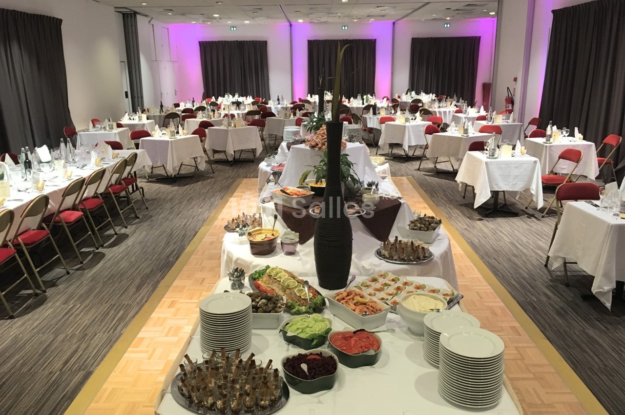Salle de réception avec tables dressées et buffet central comprenant divers plats et desserts.