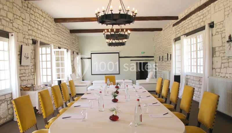 Salle de réunion lumineuse avec murs en pierre, grande table ovale entourée de chaises jaunes et écran de projection.