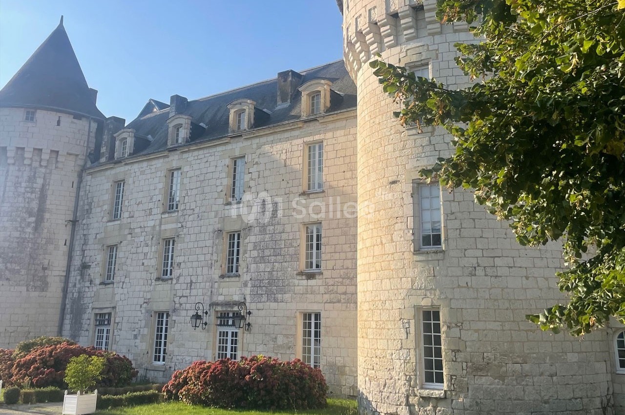Façade d'un château en pierre blanche avec tours rondes, fenêtres alignées et jardin fleuri au premier plan.