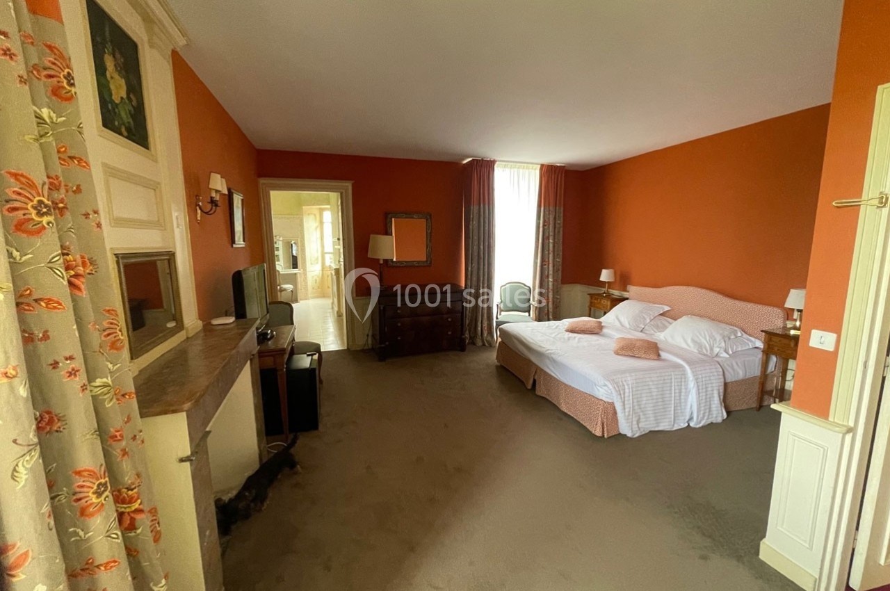 Chambre spacieuse avec murs orange, lit double, mobilier en bois, fenêtre avec rideaux et salle de bain attenante.