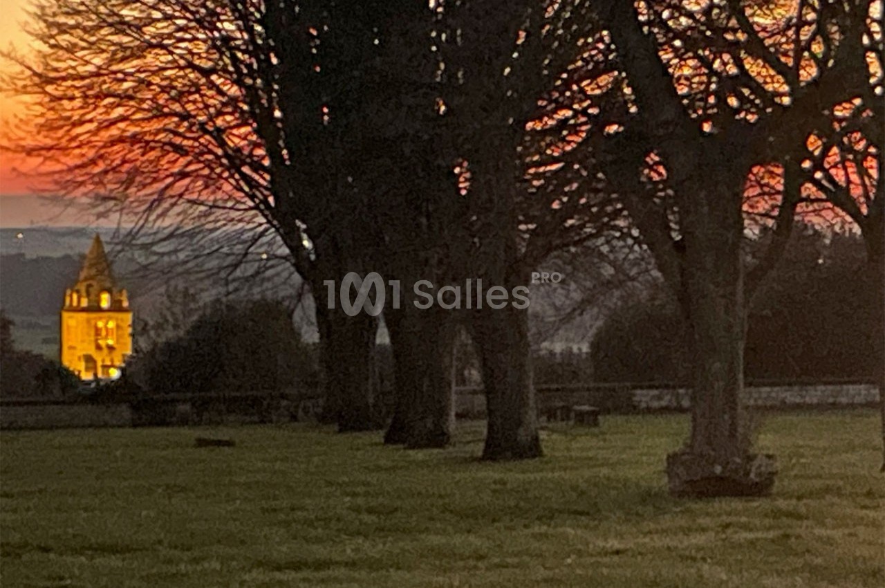 Clocher illuminé au loin, encadré par des arbres nus, sous un ciel de coucher de soleil aux teintes orangées.