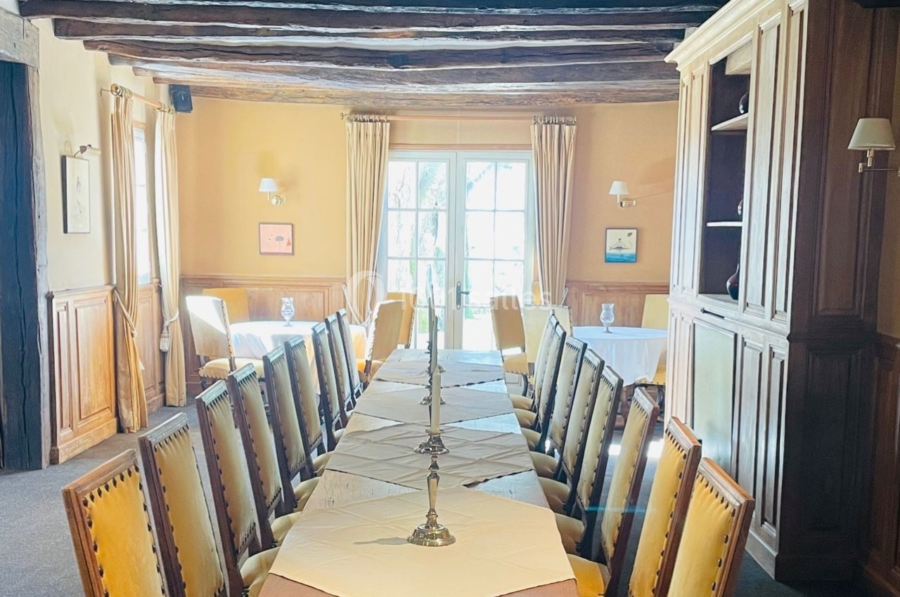 Salle à manger lumineuse avec une grande table en bois entourée de chaises, décorée de chandeliers et poutres apparentes.
