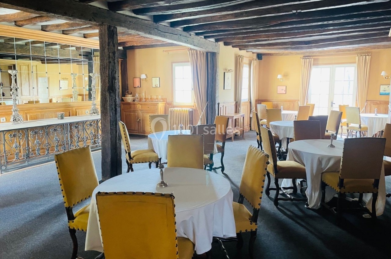 Salle de restaurant lumineuse avec des tables rondes dressées, des chaises jaunes et des poutres en bois apparentes.