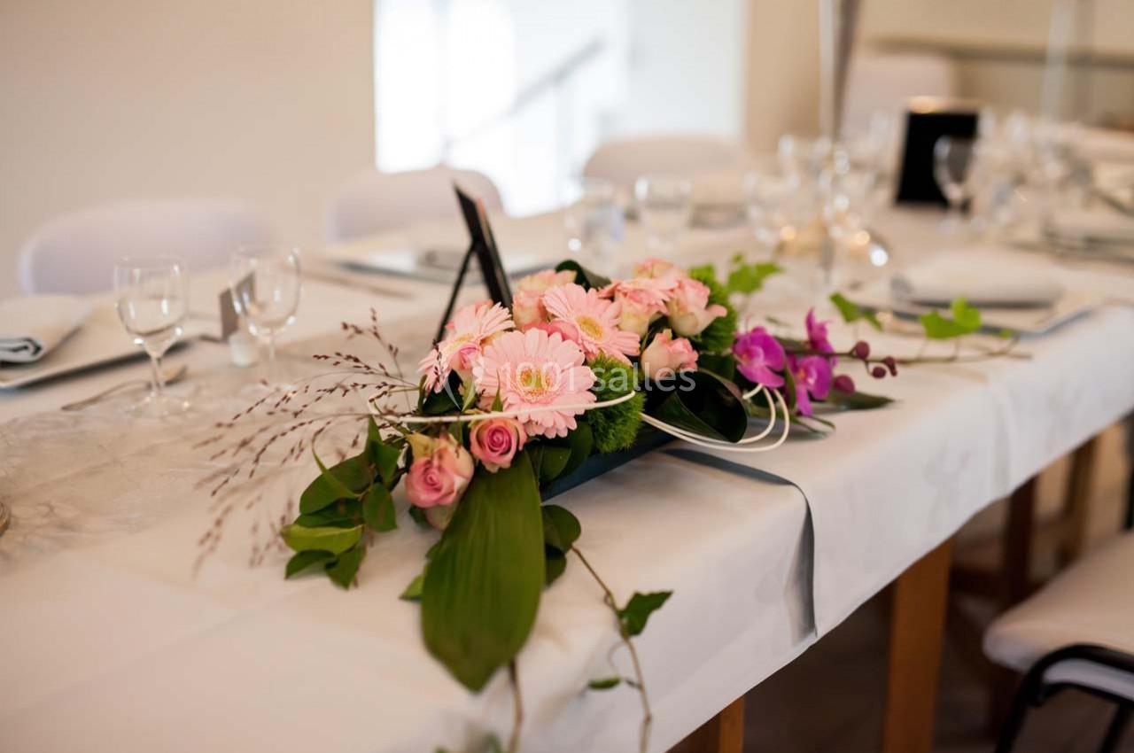 Centre de table floral avec des roses, gerberas roses et orchidées violettes sur une table dressée élégamment.
