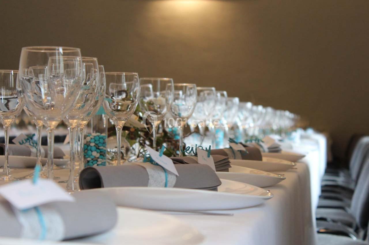 Table élégamment dressée avec des verres en cristal, des serviettes grises et des décorations bleues.