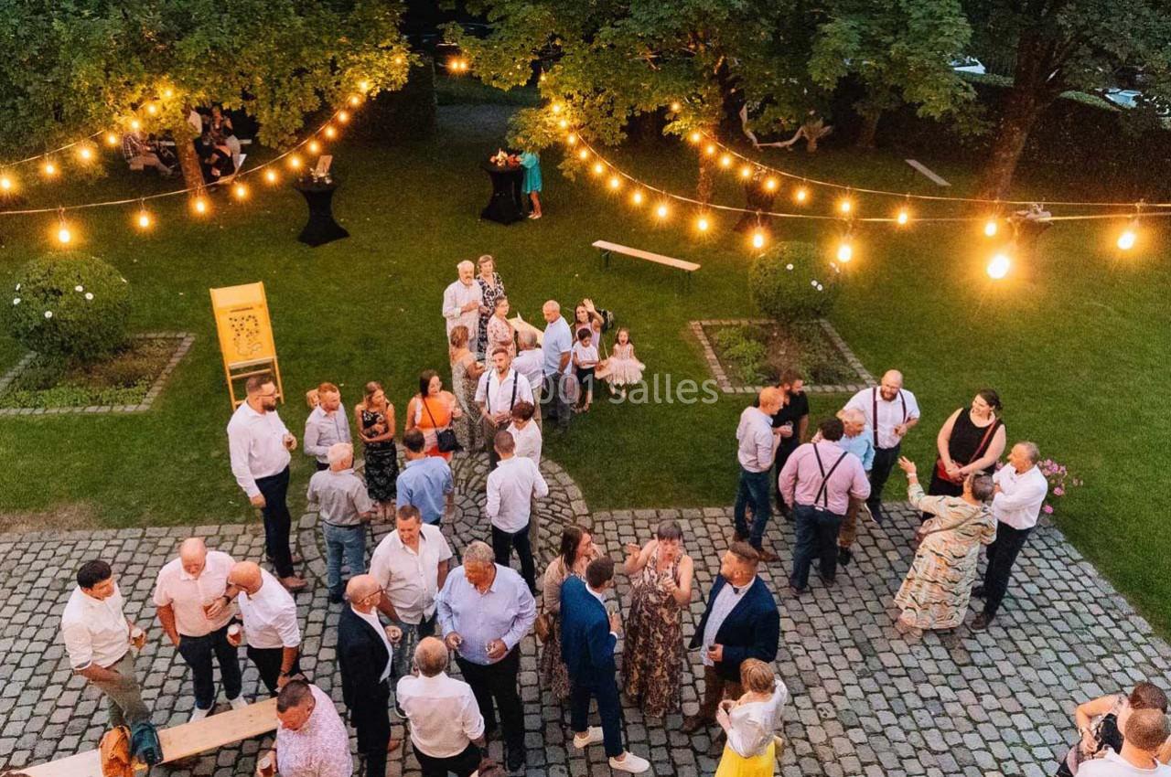 Groupe de personnes discutant lors d'un événement en plein air, éclairé par des guirlandes lumineuses dans un jardin.