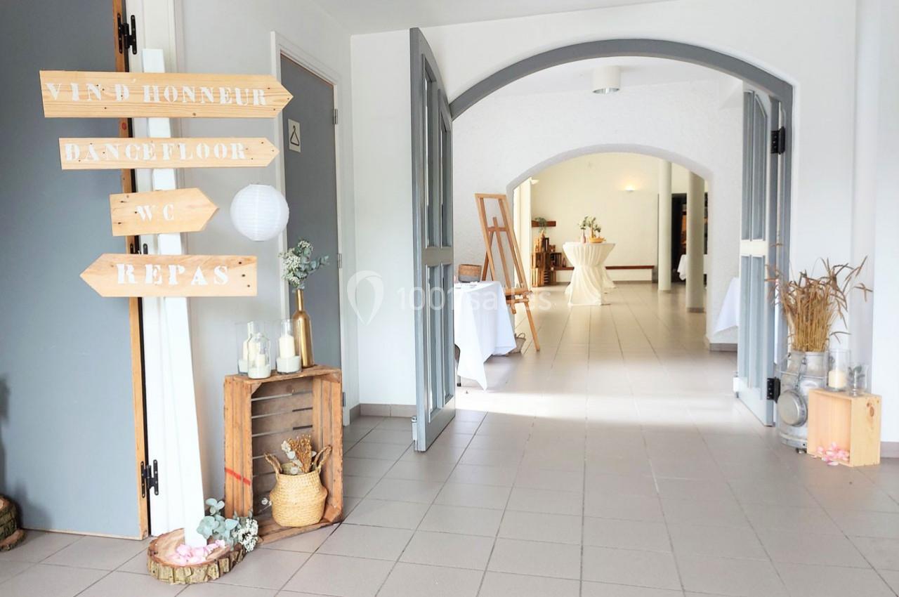 Entrée lumineuse d'une salle de réception avec panneaux directionnels en bois et décorations champêtres.