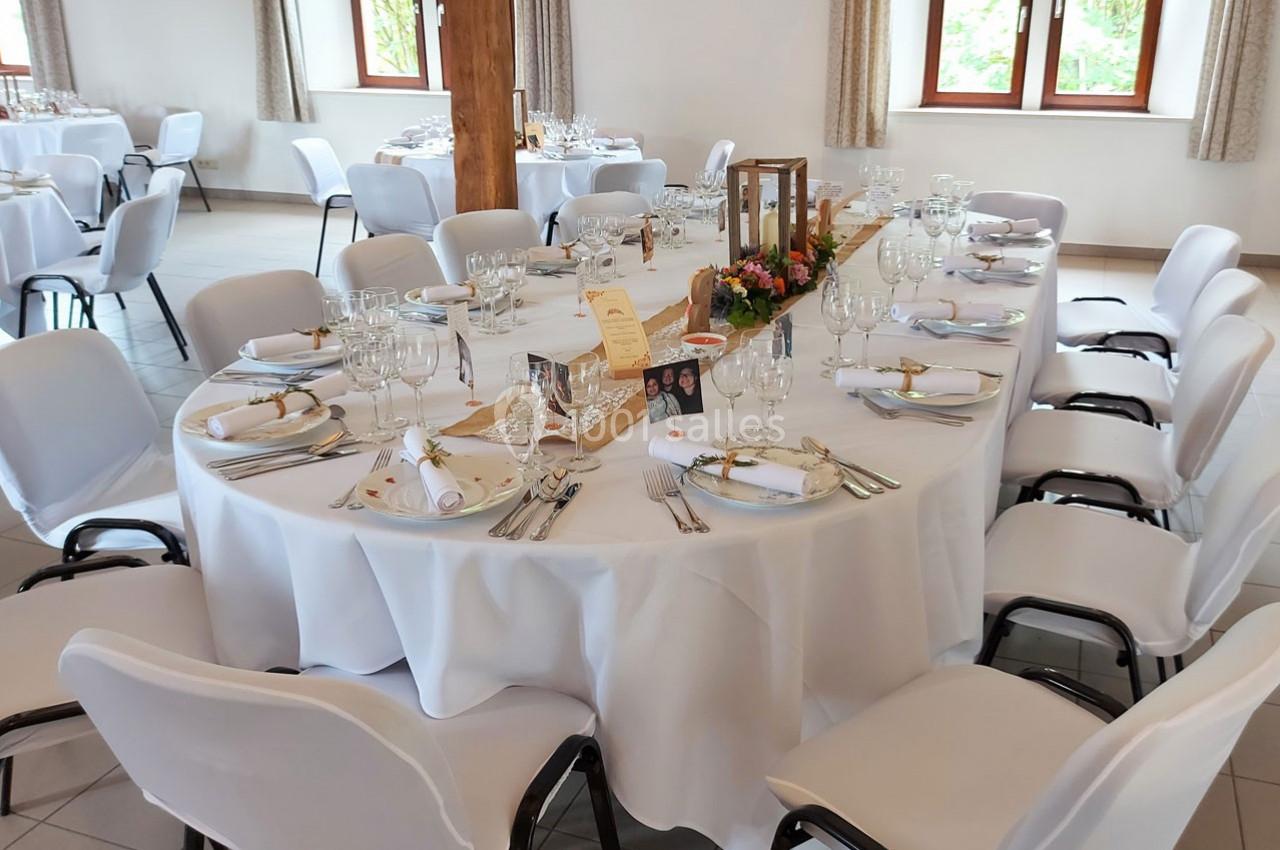 Salle de réception avec tables rondes dressées, nappes blanches, couverts élégants et décoration florale au centre.