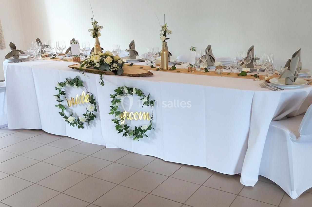 Table de mariage décorée avec nappes blanches, vaisselle élégante, fleurs et panneaux lumineux ’bride’ et ’groom’.