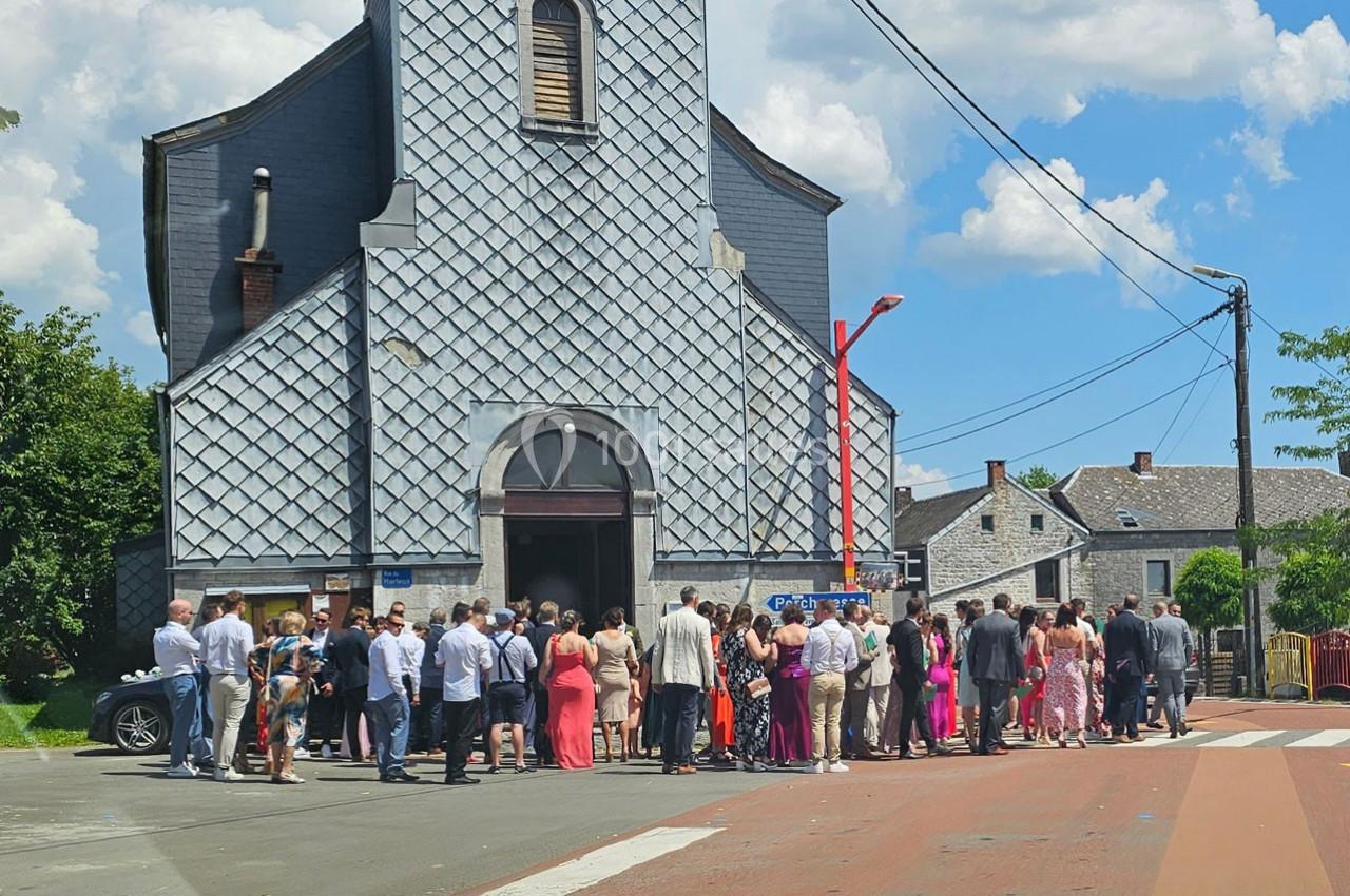 Un groupe de personnes rassemblé devant une église en pierre grise par une journée ensoleillée.