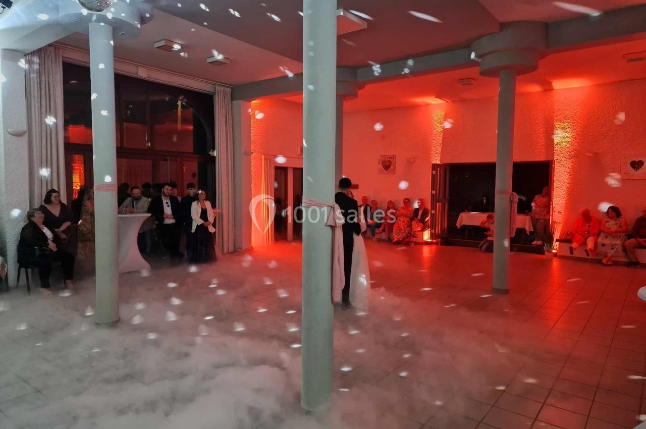 Un couple danse dans une salle éclairée de lumières rouges, entourée de fumée et de quelques invités assis.