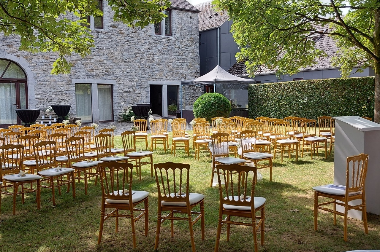 Chaises dorées disposées en extérieur sur une pelouse, devant un bâtiment en pierre, pour un événement.
