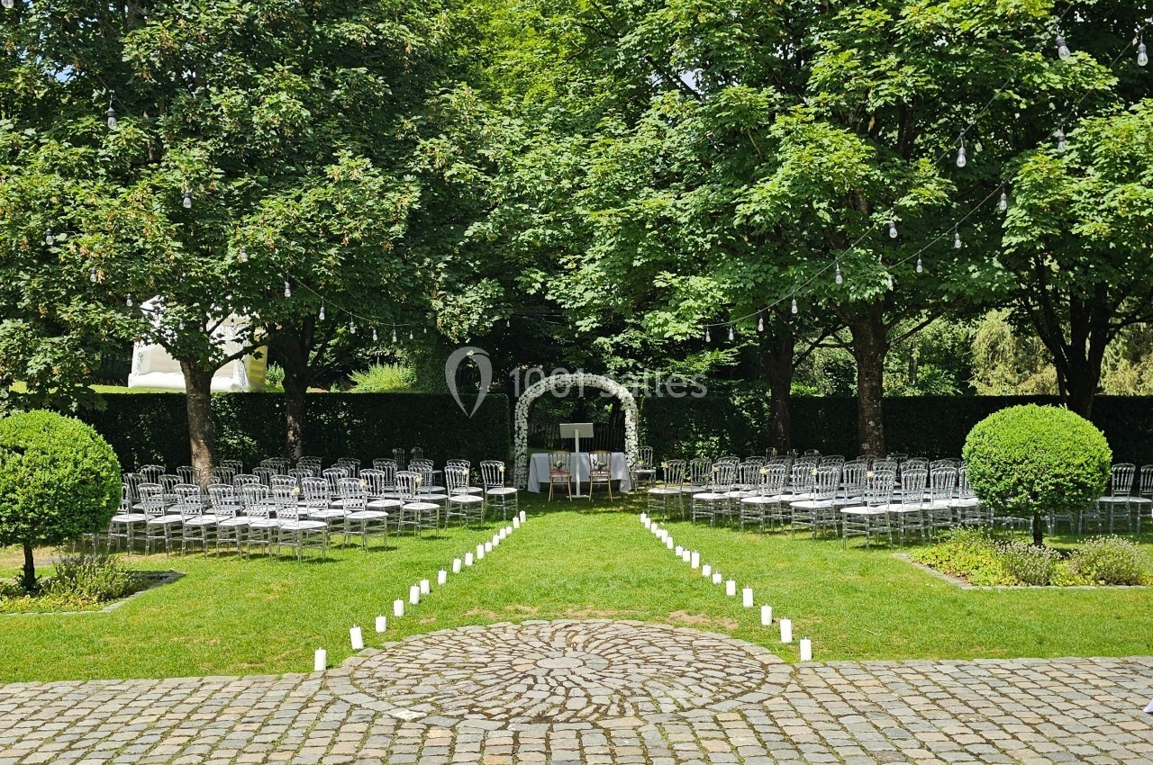 Chaises alignées en extérieur devant une arche décorative, entourées d'arbres et de verdure, pour une cérémonie.