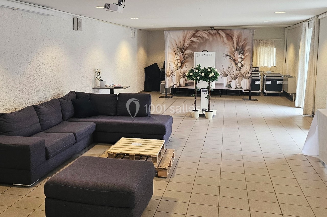 Salle lumineuse avec canapé d'angle, table basse en bois, décoration florale et espace aménagé pour un événement.
