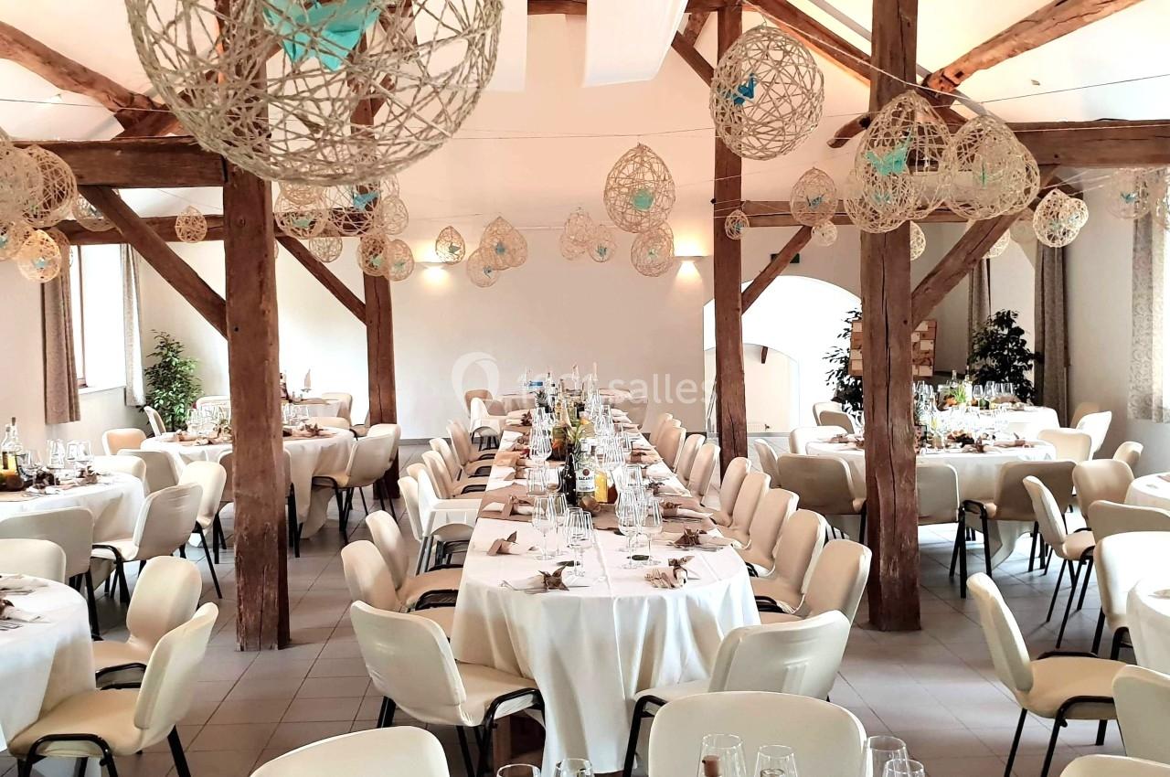 Salle de réception décorée avec des tables rondes et rectangulaires dressées, éclairée par la lumière naturelle.