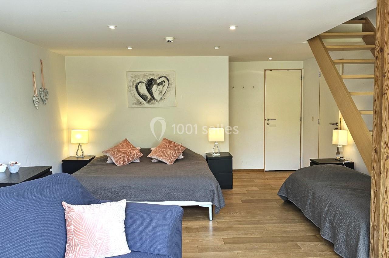 Chambre lumineuse avec deux lits, un canapé, des tables de chevet éclairées et un escalier en bois menant à un étage.