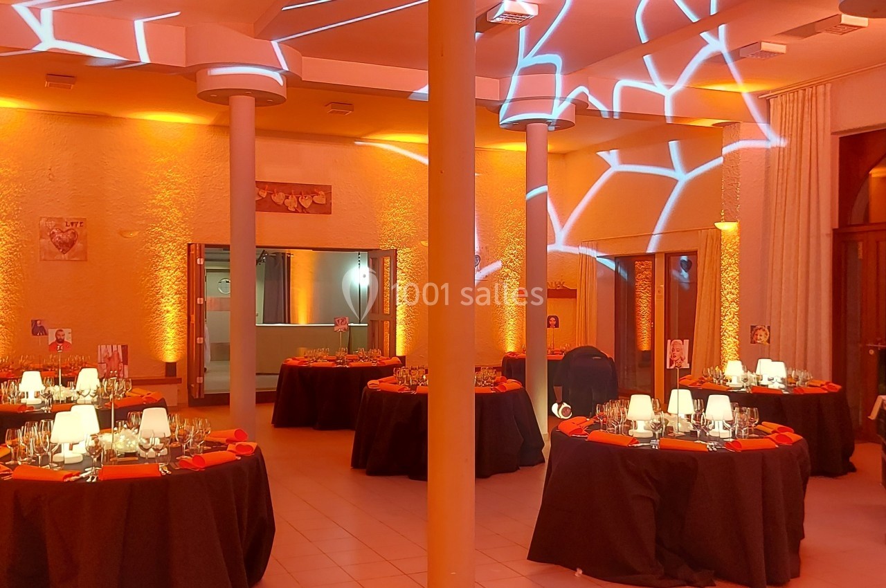 Salle de réception décorée avec des tables rondes dressées et un éclairage orange créant des motifs lumineux.
