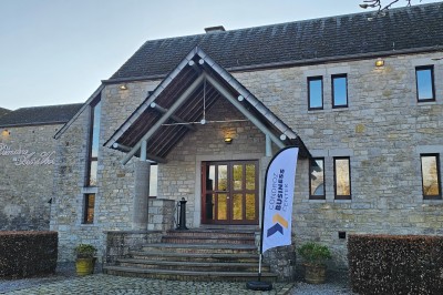 Façade d'un bâtiment en pierre avec une entrée principale, un drapeau publicitaire et une cour pavée.