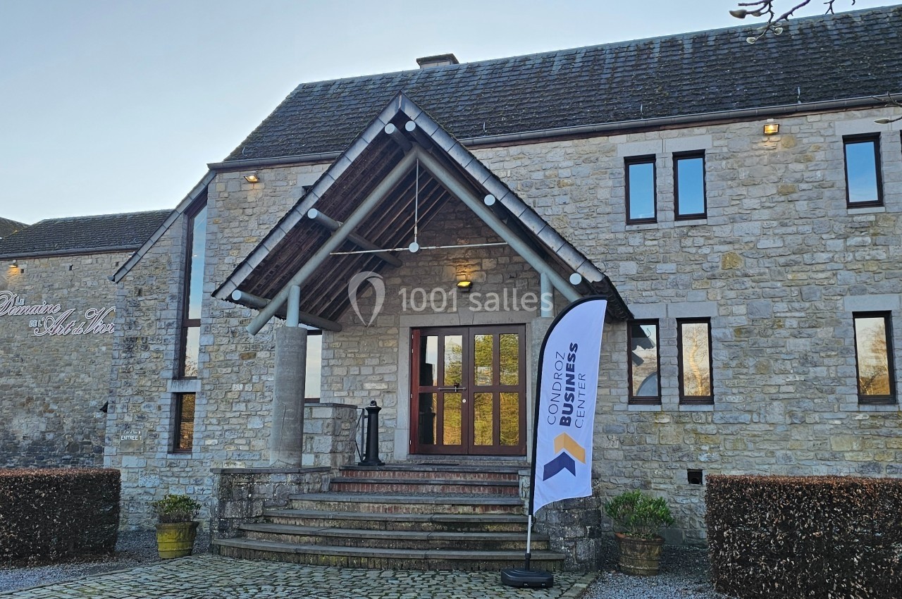 Façade d'un bâtiment en pierre avec une entrée principale, un drapeau publicitaire et une cour pavée.