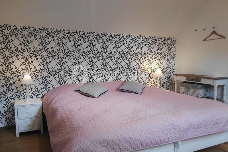Lit double avec couverture rose, deux tables de chevet blanches et une tête de lit avec motif noir et blanc.