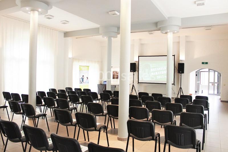 Salle de conférence lumineuse avec des rangées de chaises noires face à un écran de projection.