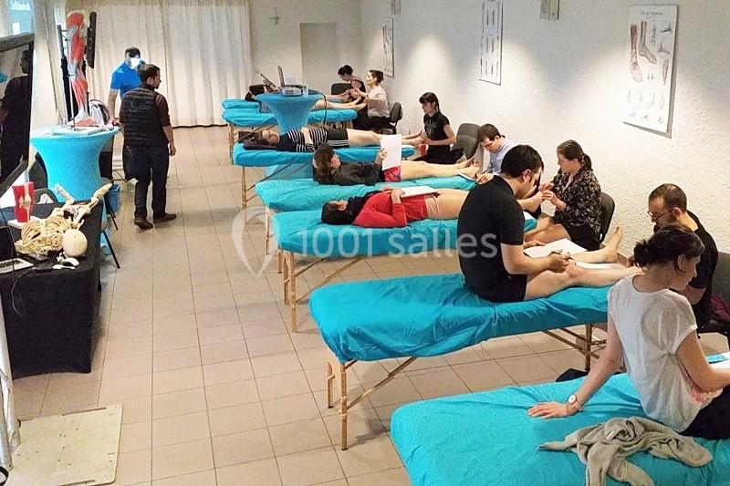 Des personnes reçoivent des massages sur des tables alignées dans une salle, sous la supervision de praticiens.