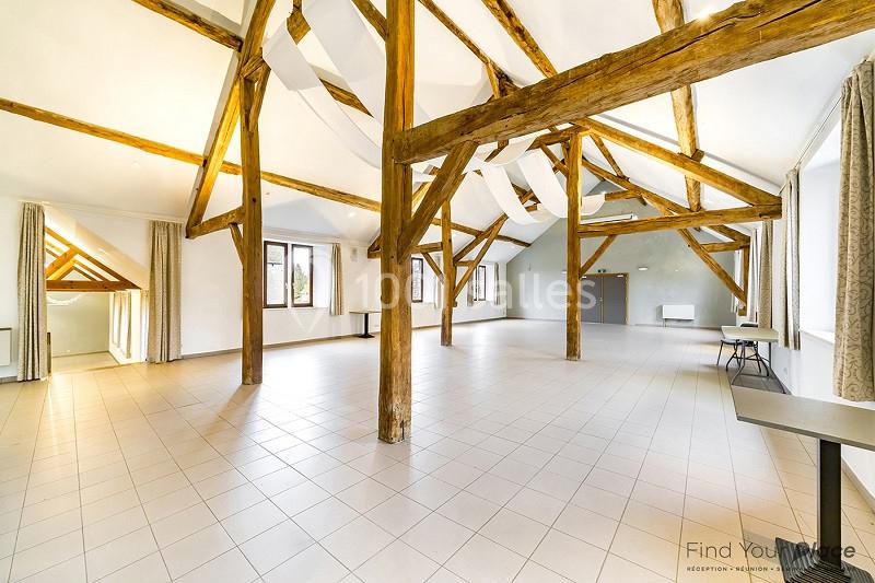 Salle spacieuse avec poutres apparentes, carrelage clair, grandes fenêtres et rideaux, éclairée par la lumière naturelle.