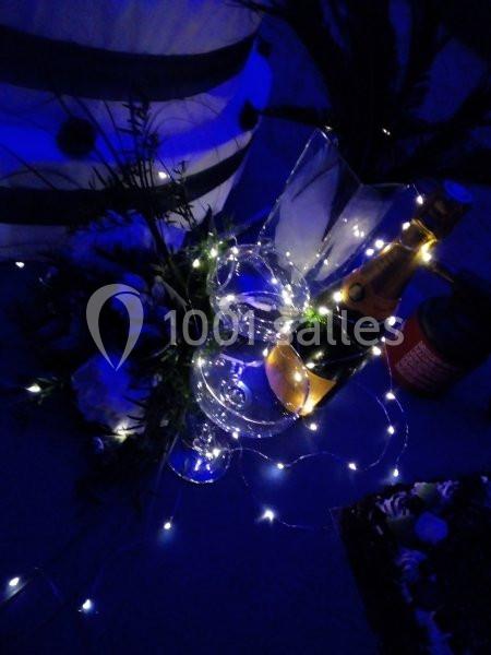 Location salle Beaudéduit (Oise) - LFK Réceptions #16 Bouteille de champagne, flûtes et décorations lumineuses sur une table dans une ambiance tamisée bleutée.