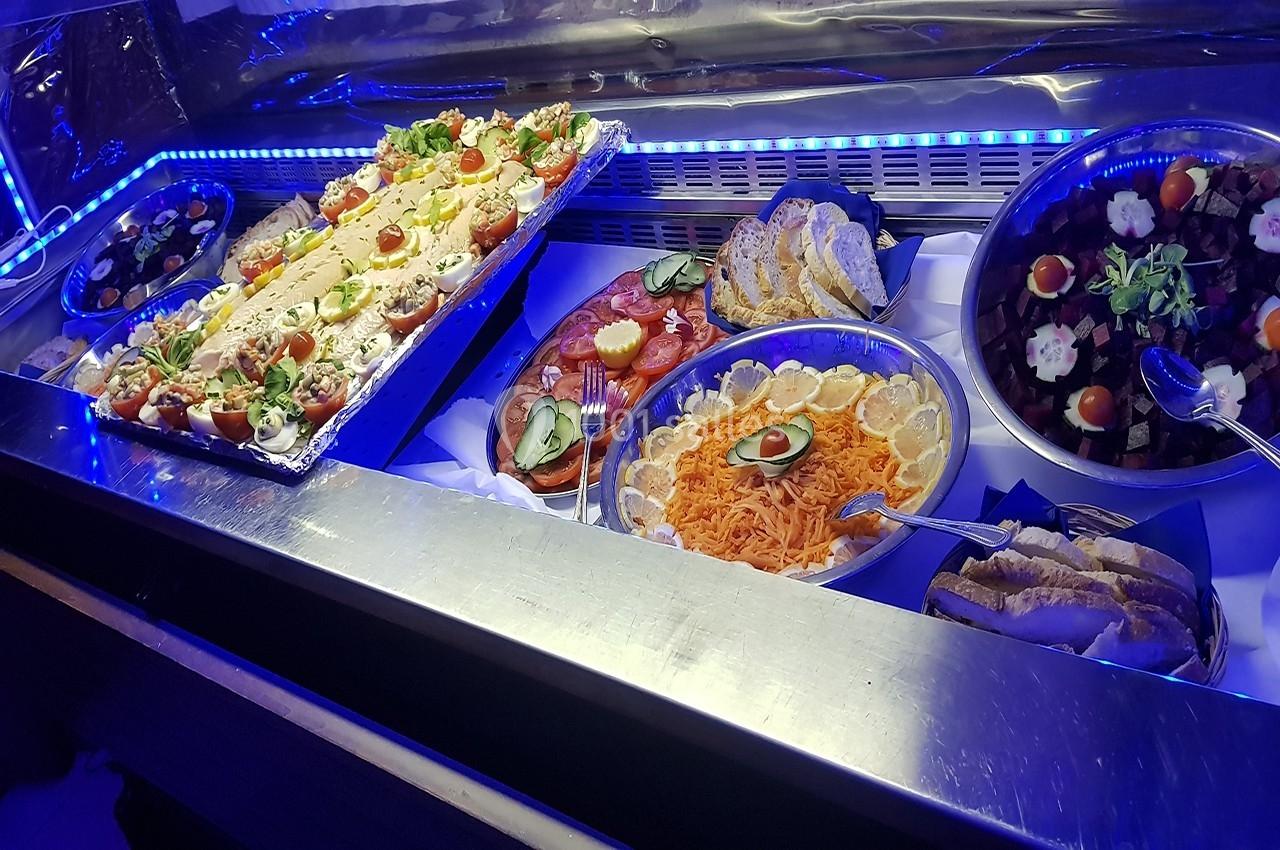 Location salle Beaudéduit (Oise) - LFK Réceptions #19 Buffet froid avec plats variés : salades, légumes, charcuterie, pain et garnitures, présenté sous éclairage bleu.